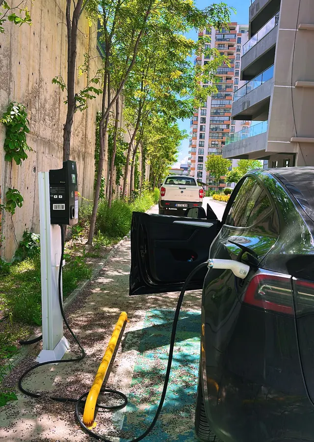 Bir konut sitesinin bahçesinde direğe monte AC şarj cihazına bağlı elektrikli otomobil