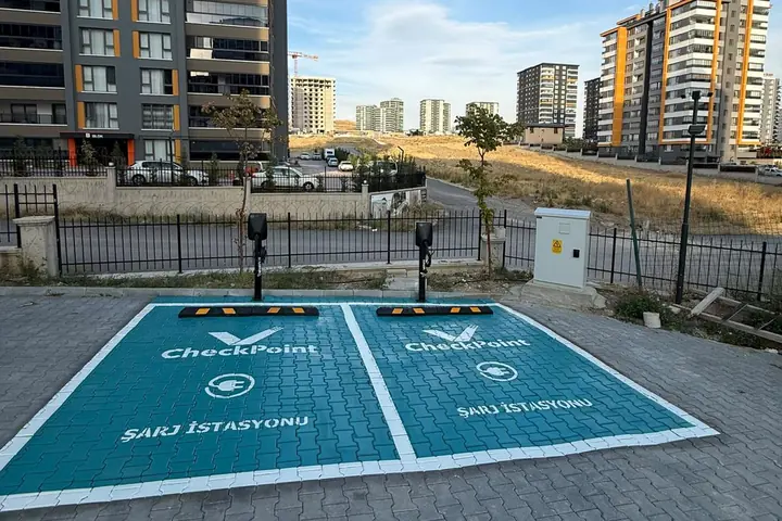 Konut bloklarının önünde turkuaz zeminli iki AC şarj yeri