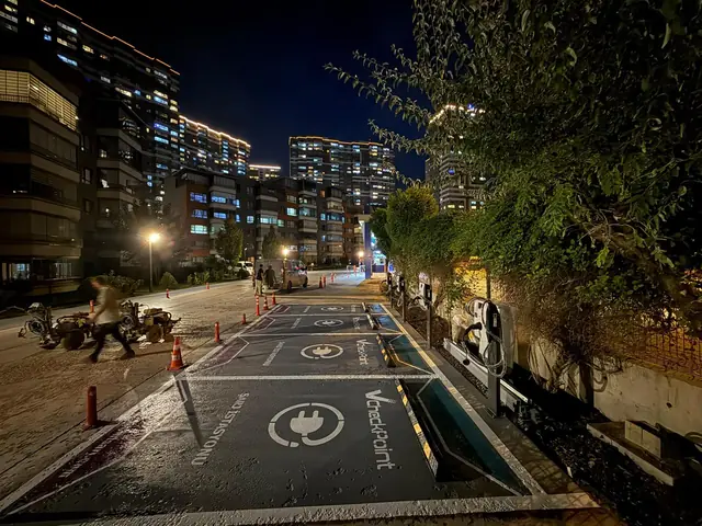 Gece çekilmiş bir konut sitesi girişinde art arda şarj yerleri ve duvara monte AC şarj cihazları