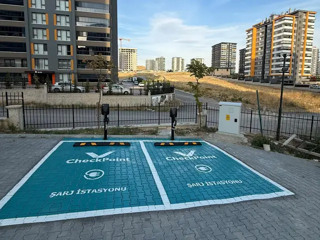 Konut bloklarının önünde turkuaz zeminli iki AC şarj yeri